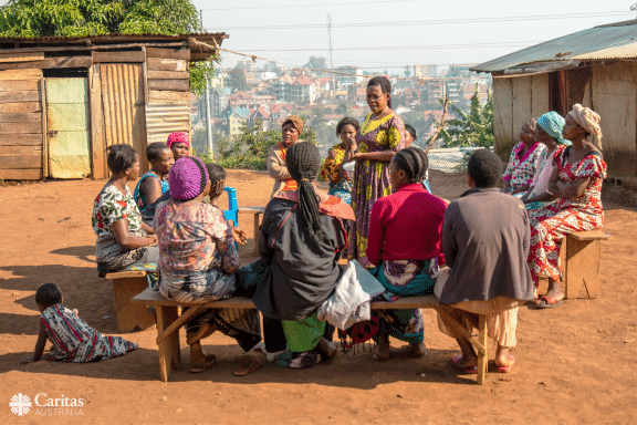 A group of people who are sitting on benches outside simple dwellings