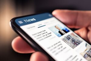 Image of a hand holding a mobile phone with a news feed image